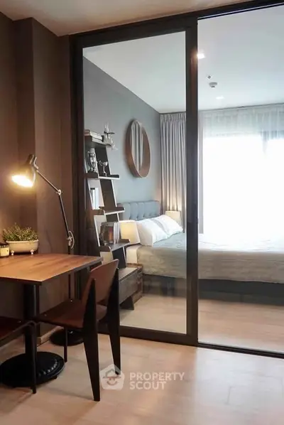 Modern bedroom with study area, featuring sleek furniture and natural light through large windows.