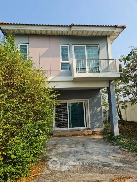 Charming two-story house with a small balcony and lush greenery, perfect for family living.