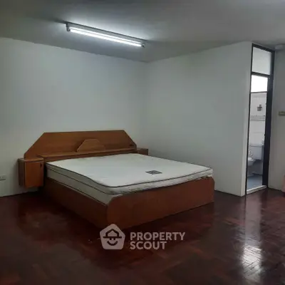 Spacious bedroom with wooden flooring and attached bathroom in modern apartment.