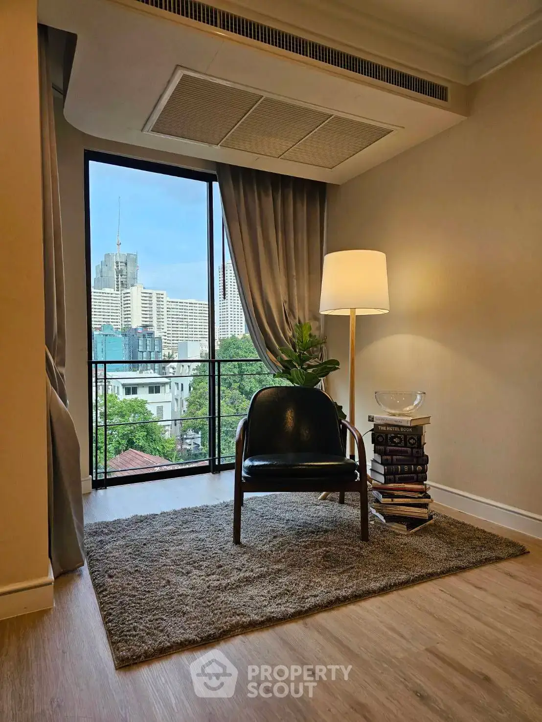 Stylish reading nook with city view, featuring a cozy chair, floor lamp, and plush rug in a modern apartment.