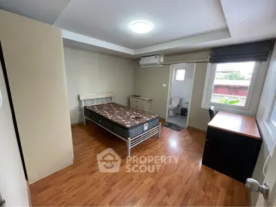 Spacious bedroom with wooden flooring and natural light, featuring a bed, desk, and air conditioning.