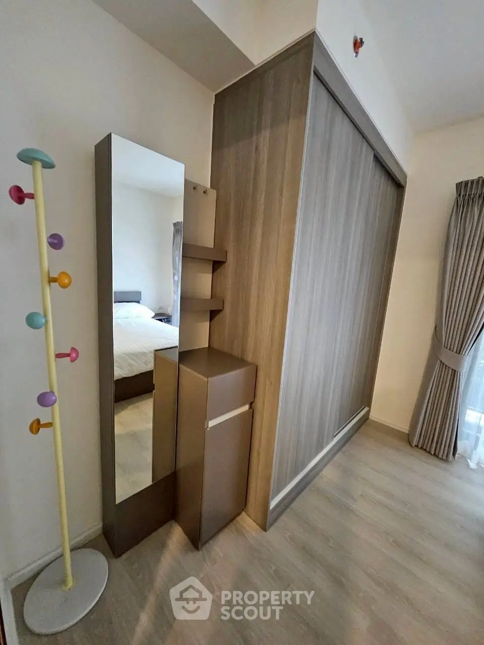 Modern bedroom with stylish wardrobe and full-length mirror, featuring elegant curtains and wooden flooring.