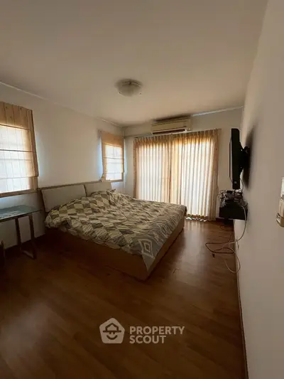 Spacious bedroom with large windows and wooden flooring, featuring a cozy bed and modern decor.