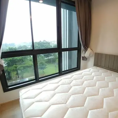 Bright bedroom with large windows offering a serene garden view, featuring a comfortable mattress and elegant curtains.