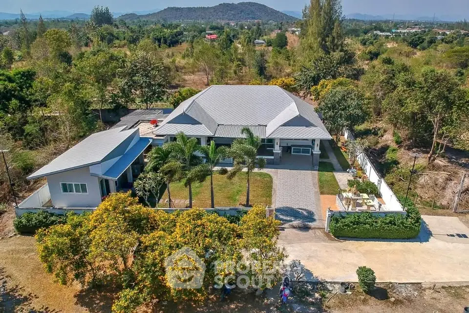 Stunning aerial view of a spacious countryside villa with lush gardens and mountain backdrop.