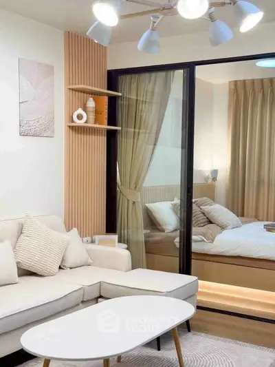 Modern living room with cozy sofa and view into elegant bedroom through glass partition.