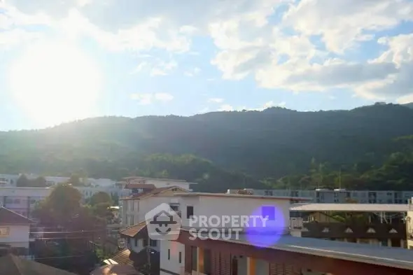 Scenic view of residential buildings against a backdrop of lush green hills and a bright sky.