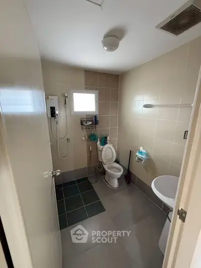 Modern bathroom with sleek fixtures and neutral tiles, featuring a shower and toilet in a compact layout.