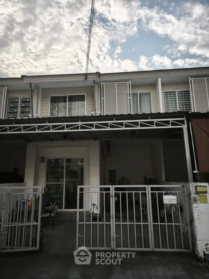 Charming two-story townhouse with gated entrance and modern facade under a picturesque sky.