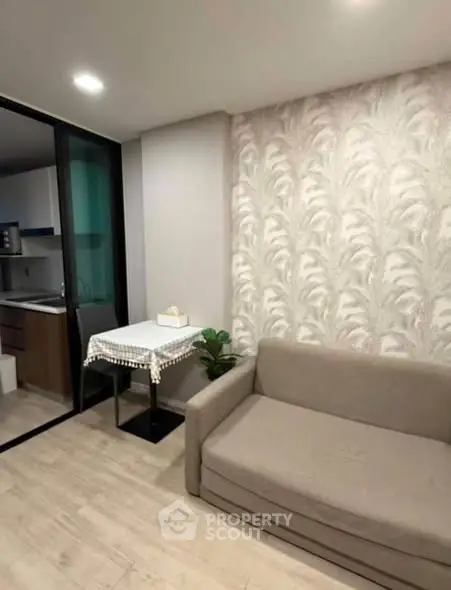 Modern living room with stylish wallpaper and cozy sofa, adjacent to a compact kitchen area.