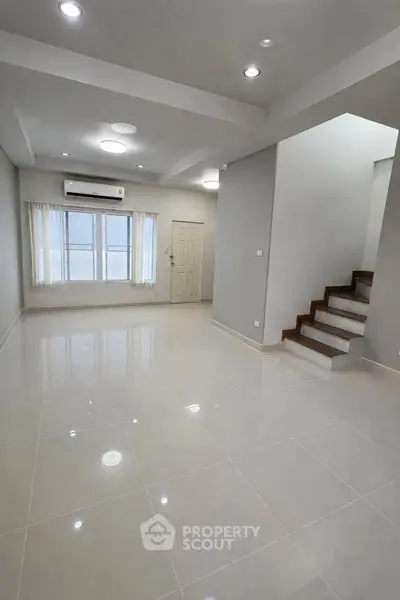 Spacious modern living room with sleek tile flooring and staircase, perfect for contemporary living.