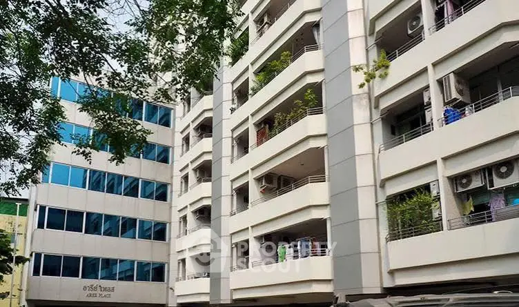 Modern apartment building with balconies and lush greenery in urban setting.