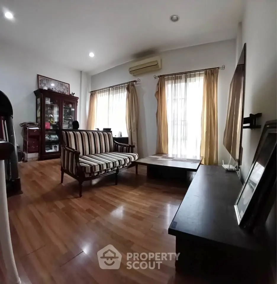 Charming living room with wooden flooring, elegant furniture, and natural light from large windows.