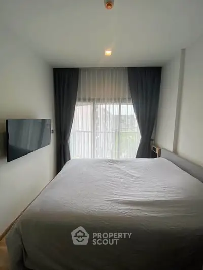 Cozy bedroom with large window and wall-mounted TV, perfect for relaxation.