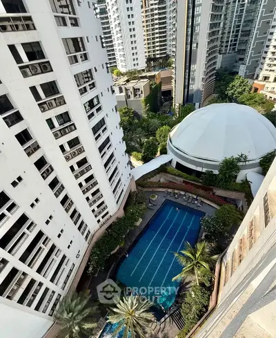 Stunning aerial view of luxury condominium with pool and lush greenery in urban setting.