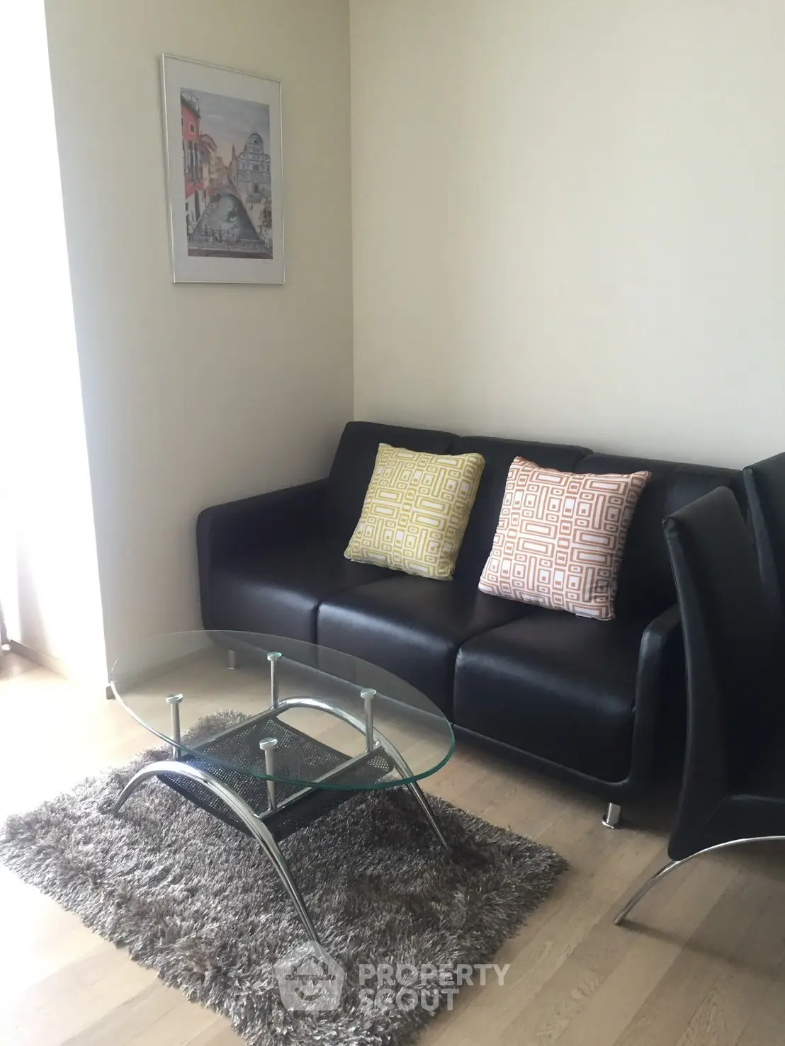 Modern living room with sleek black sofa and glass coffee table on plush rug.