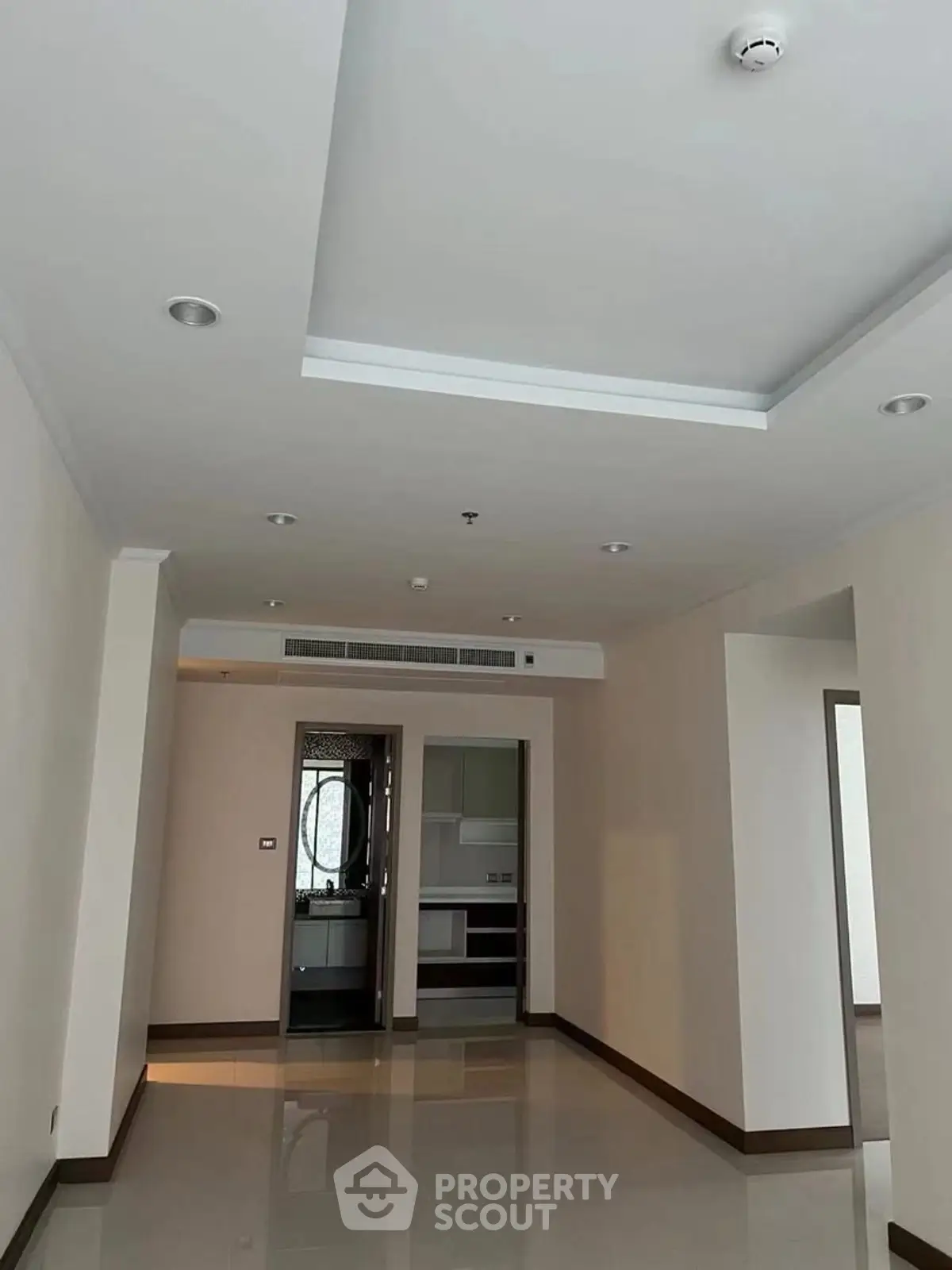 Spacious modern living room with sleek ceiling design and glossy floors, leading to a contemporary kitchen.