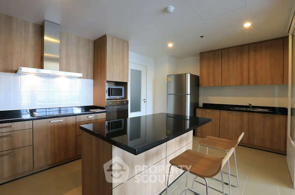 Modern kitchen with sleek wooden cabinets and island, featuring stainless steel appliances and elegant lighting.