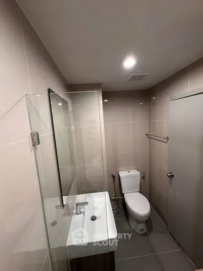 Modern bathroom with sleek design, featuring a glass shower, white sink, and toilet in a compact layout.