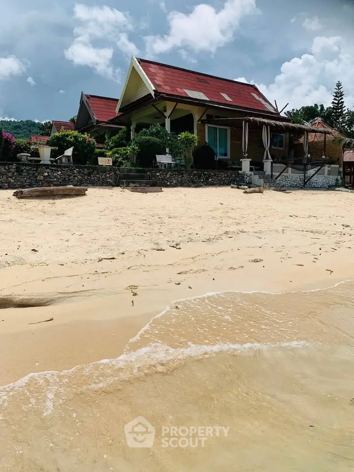 Charming beachfront property with red roof and lush garden, perfect for serene coastal living.