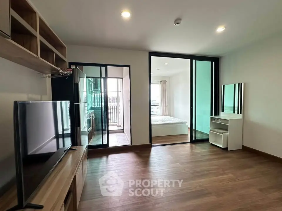 Modern apartment interior with open living room and bedroom, featuring wooden flooring and sleek design.