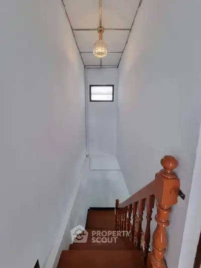Charming staircase with wooden railing and elegant chandelier in a cozy home setting.