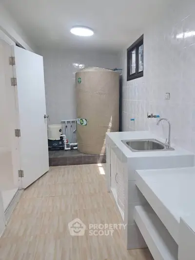 Spacious utility room with water tank and sink, ideal for storage and laundry tasks.