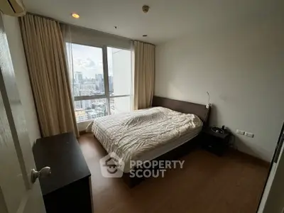 Cozy bedroom with city view, featuring a large window and modern furnishings.