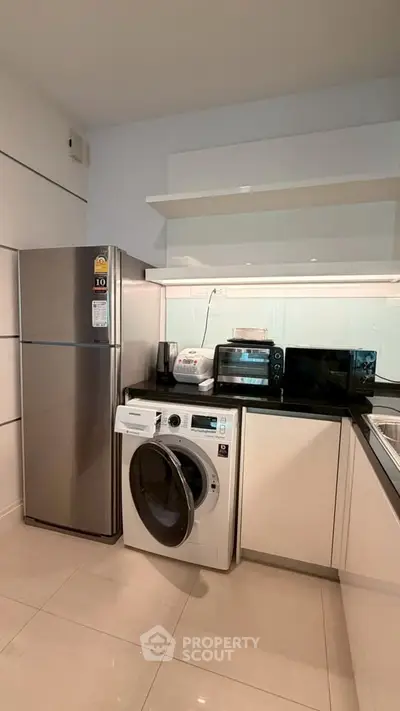 Modern kitchen with stainless steel fridge, washing machine, and sleek white cabinetry.