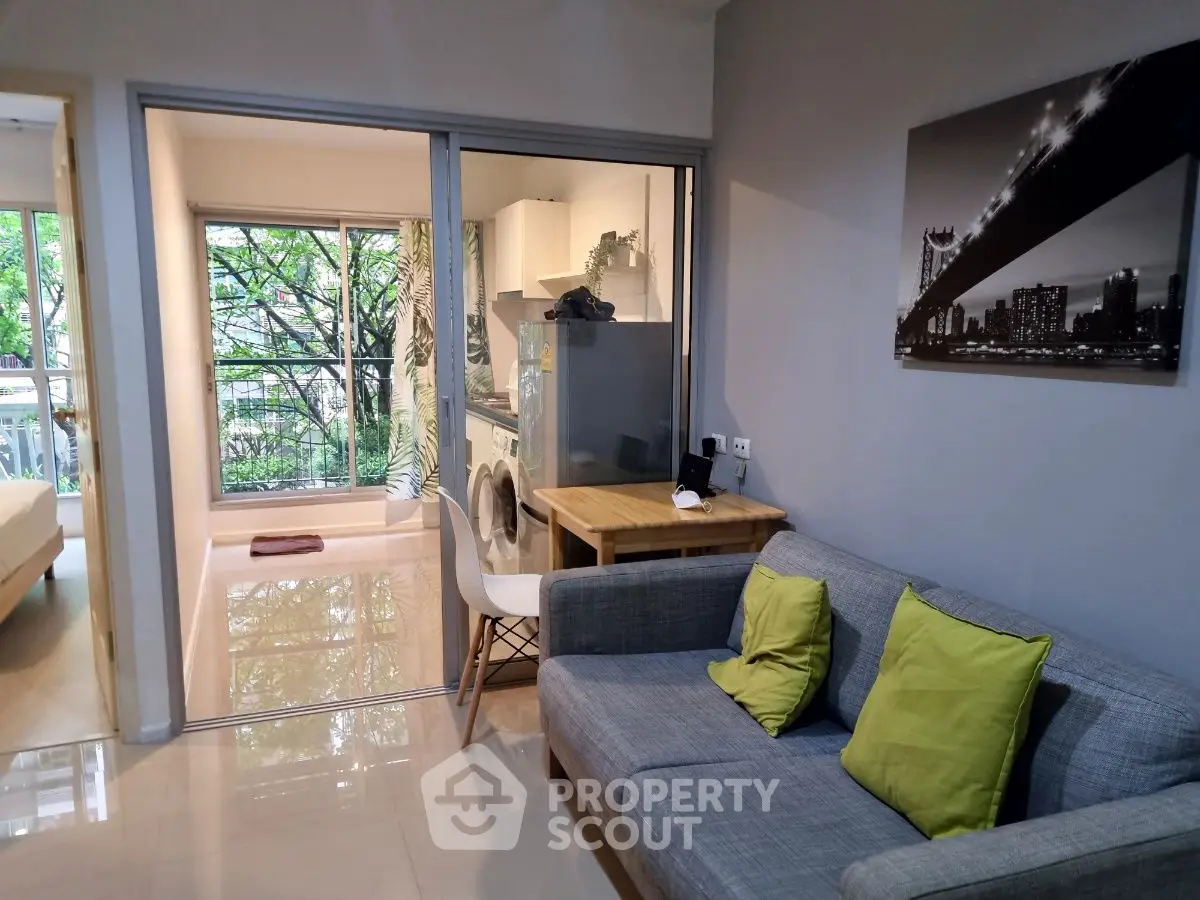 Modern living room with cozy sofa and open kitchen layout, featuring a washing machine and large windows.