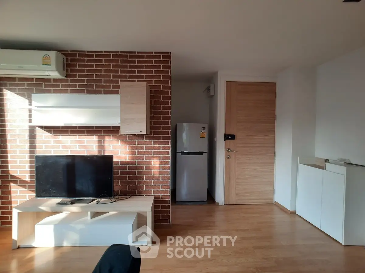 Modern living room with brick accent wall, TV unit, and sleek wooden flooring.