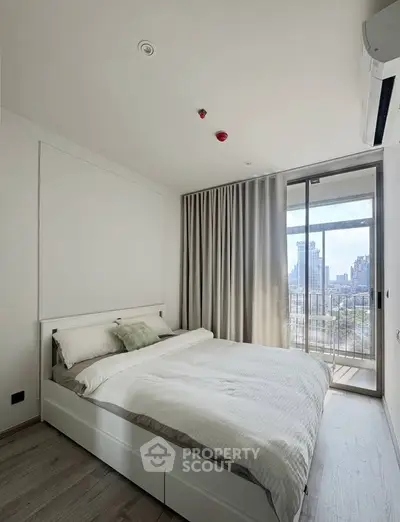 Modern bedroom with city view and balcony access, featuring minimalist design and natural light.