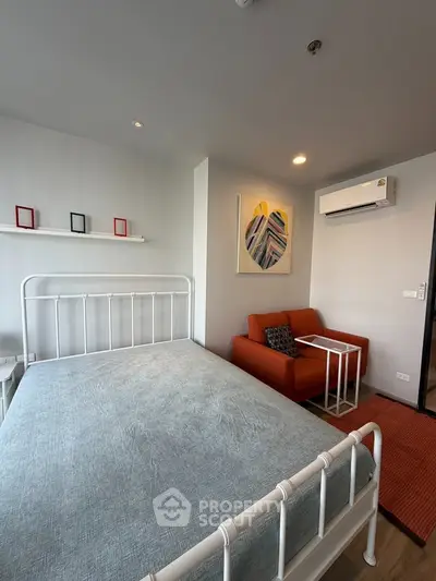 Modern bedroom with stylish decor and cozy seating area, featuring a sleek metal bed frame and vibrant artwork.