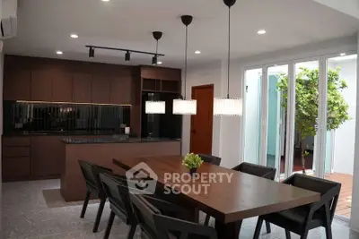 Modern kitchen with open layout and stylish dining area, featuring sleek lighting and a view of the patio.
