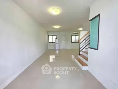 Spacious modern living room with sleek staircase and bright natural lighting.