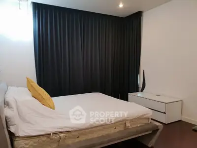 Modern bedroom with sleek design and dark curtains, featuring a comfortable bed and stylish furniture.
