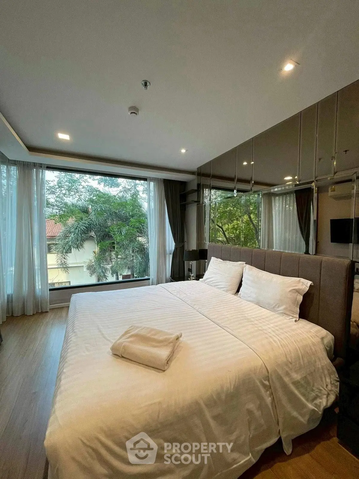 Luxurious bedroom with large windows offering a serene garden view, featuring modern decor and plush bedding.