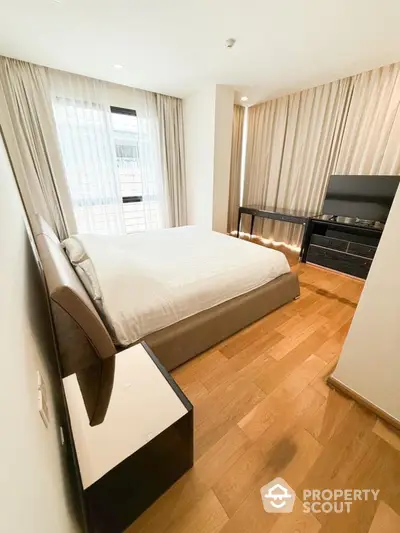 Modern bedroom with wooden flooring and large window, featuring elegant curtains and a sleek TV stand.