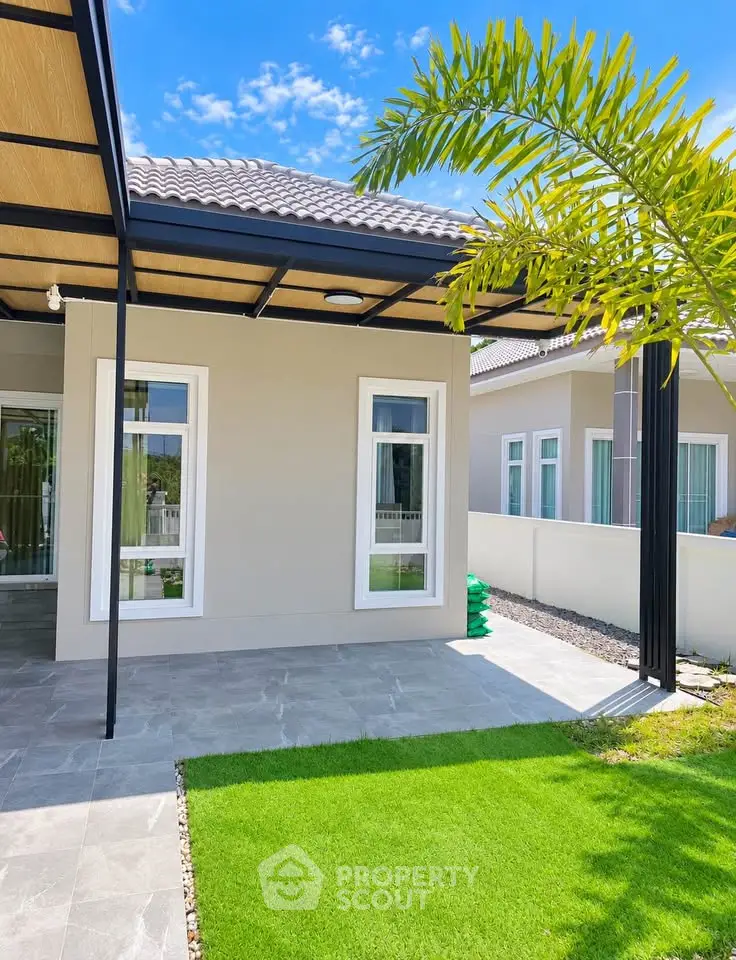 Modern house exterior with lush green lawn and sleek architectural design under a clear blue sky.