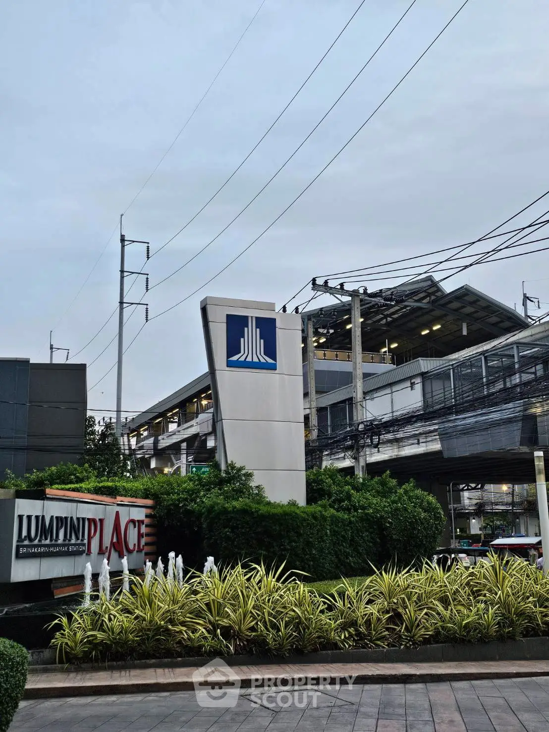 Modern urban residential building entrance with lush landscaping and prominent signage.