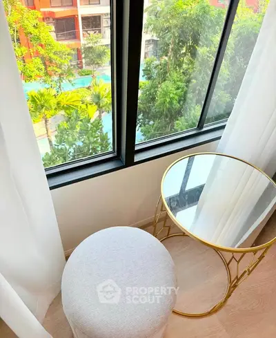 Bright room with elegant decor and pool view, featuring a stylish round table and plush stool by the window.