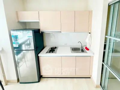 Modern compact kitchen with sleek cabinetry and stainless steel fridge in a bright apartment.