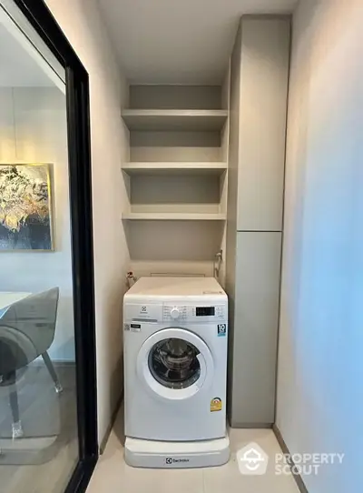 Compact laundry area with modern washing machine and built-in shelves in a sleek apartment.