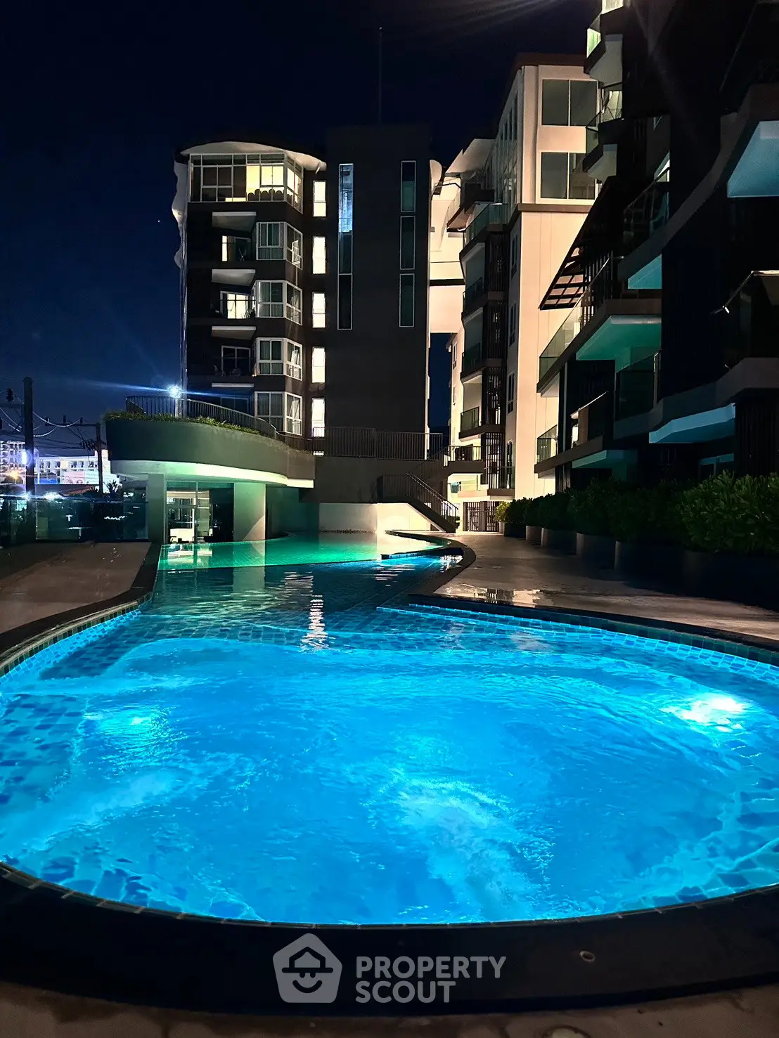 Luxurious apartment complex with illuminated pool at night, showcasing modern architecture and serene ambiance.