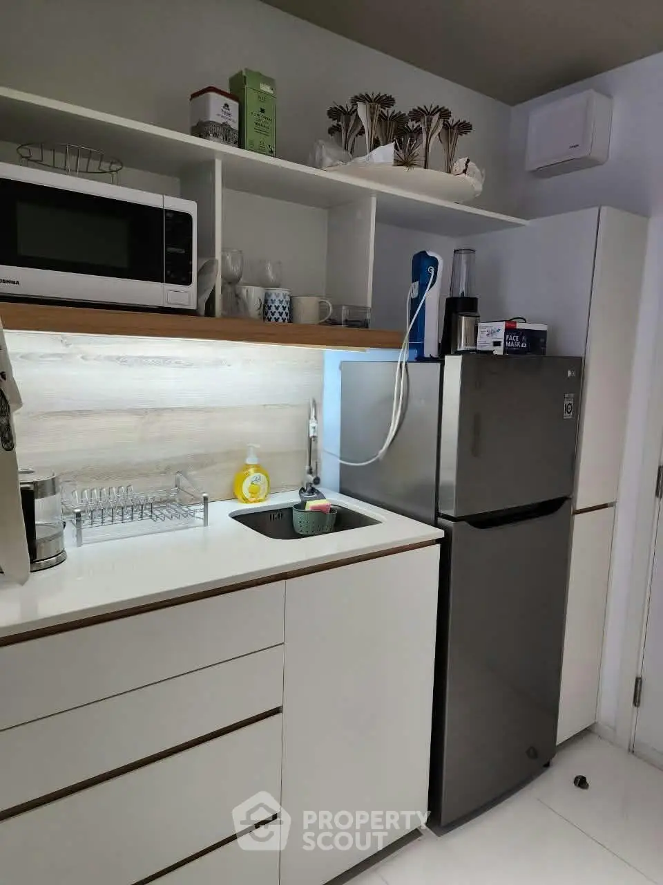 Modern kitchen with sleek white cabinets, stainless steel fridge, and microwave, perfect for urban living.