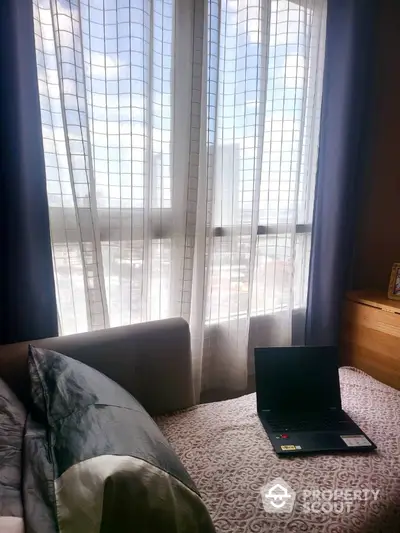 Cozy bedroom with natural light and city view, perfect for relaxation and work-from-home setup.