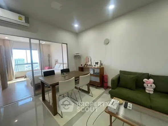Modern open-plan living room with dining area and bedroom view, featuring stylish furniture and bright lighting.
