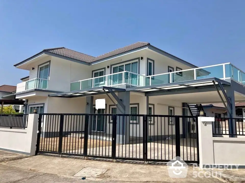 Modern two-story house with sleek balcony and gated entrance in sunny neighborhood.