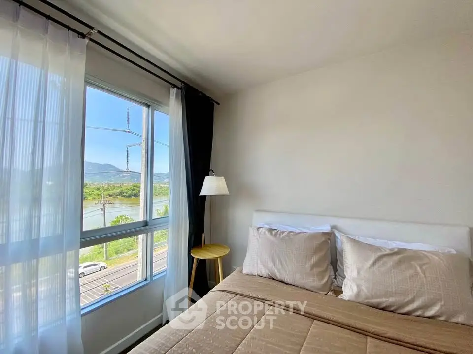 Bright bedroom with large window offering scenic mountain and river views, cozy bed setup.