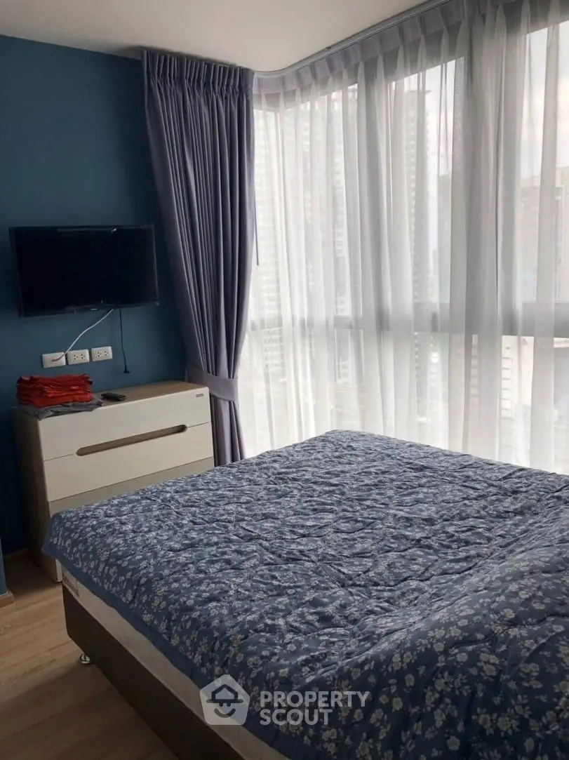 Cozy bedroom with large windows and blue floral bedding in modern apartment.